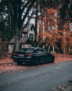 a black car parked on the side of a road in front of trees with leaves all over it