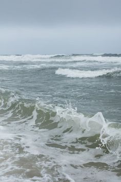 an ocean with waves crashing on the shore and one person standing in the water holding a surfboard