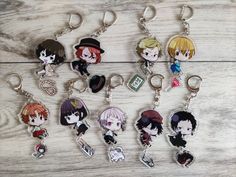 seven anime keychains are shown on a wooden surface, each with an image of the same character