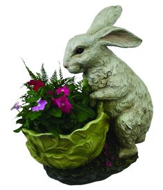 a white rabbit statue sitting on top of a green planter filled with purple and red flowers