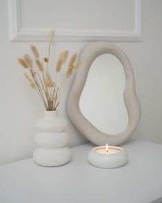 a white vase sitting on top of a table next to a mirror and a lit candle