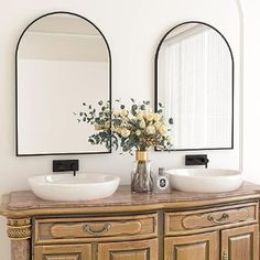 there are two sinks in the bathroom with mirrors on the wall above them and vases filled with flowers