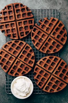 three waffles on a cooling rack with whipped cream in a bowl next to them