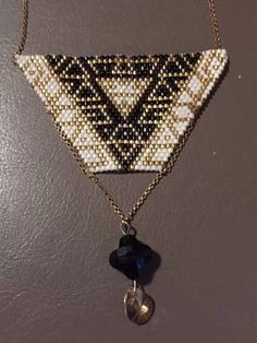 the beaded triangle is hanging from a gold chain with a black and white pendant