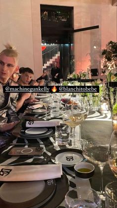 a group of people sitting at a long table with plates and wine glasses on it