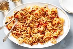 a white plate topped with pasta and shrimp next to two glasses of wine on a table