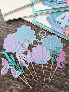 mermaid cupcake toppers and cake picks are sitting on a table next to each other