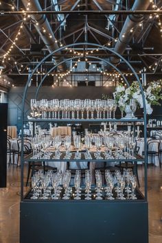 This image features a white bloom and greenery floral arrangment on a black champagne rack. This is for a wedding cocktail hour. The arrangement is in a grey stone urn. Italian Village, Moments Photography, Reception Area, Reception Areas