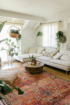 a living room filled with lots of furniture and plants on top of a rug in front of a window