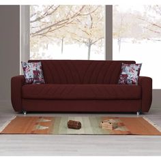 a red couch sitting on top of a wooden floor next to a rug and window