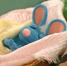 a stuffed animal is laying in a basket with a blanket on it's side