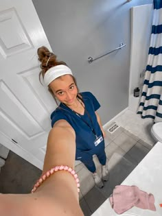 a woman in scrubs taking a selfie in the bathroom with her hand out