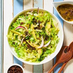 a white bowl filled with lettuce, onions and olives next to two bowls of sauce