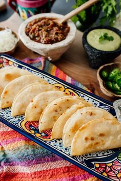 six tortillas on a plate with salsa and guacamole in the background