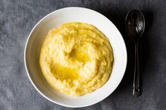 a bowl of mashed potatoes with a spoon next to it on a gray surface