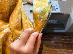 a person is sewing fabric on a piece of cloth with a sewing machine in the background