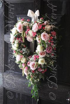 a heart - shaped wreath with pink and white flowers hangs on the front door of a house