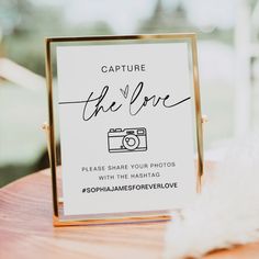 a sign that says capture the love on top of a wooden table next to a white feather