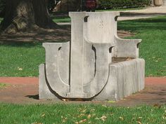 a cement bench sitting on top of a lush green grass covered park area next to a tree