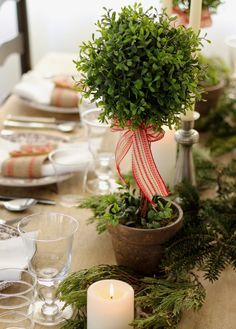 the table is set for christmas with candles and greenery in pots on each side