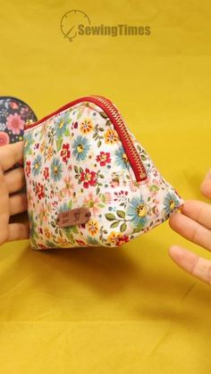 two hands are holding a small floral purse