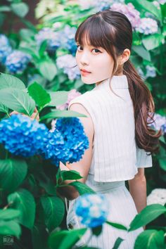 a woman standing in front of blue flowers