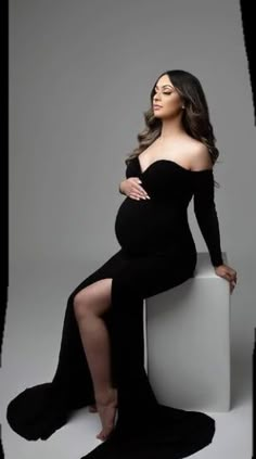 a pregnant woman sitting on top of a white block with her legs crossed and wearing black