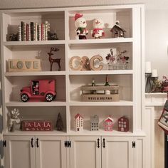 a white bookcase filled with lots of books and toys next to a christmas tree