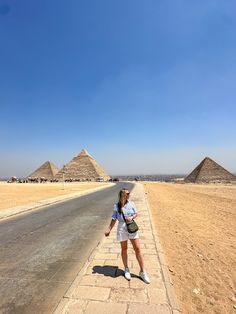 a woman standing on the side of a road in front of three pyramids