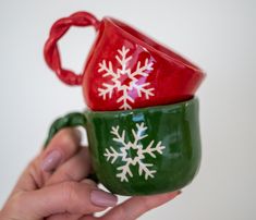 two green and red mugs with snowflakes painted on them, one being held by a hand