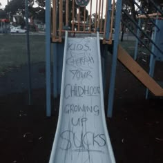 a slide with graffiti written on it in a park area next to a play structure