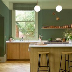 a kitchen with green walls and wooden flooring, two stools at the island