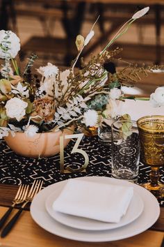 the table is set with white plates and silverware, gold cutlery, and floral centerpieces