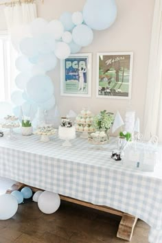 a table topped with lots of blue and white balloons next to a wall filled with pictures