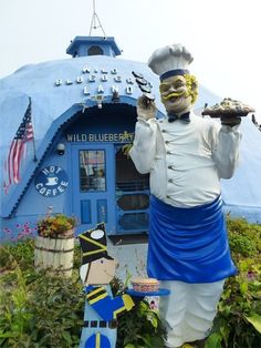 a statue of a chef holding a tray in front of a blue building with an american flag on it