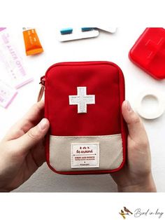 a person holding a red first aid kit in their left hand and other medical supplies on the table