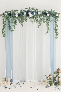 a white table topped with candles and flowers next to a blue drape covered wall