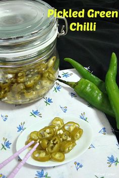 pickled green chilli on a plate next to a jar with hot peppers in it