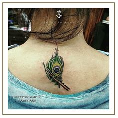 the back of a woman's neck with a peacock feather on it and an arrow tattoo