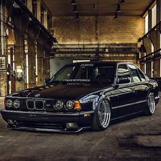 a black bmw is parked in an old warehouse with its hood up and lights on