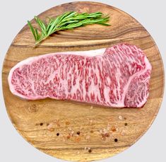 a piece of raw meat sitting on top of a wooden cutting board next to a sprig of rosemary