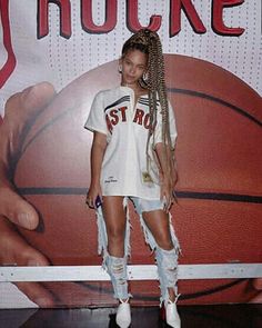 a woman standing in front of a basketball with braids on her head and white shirt