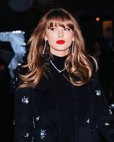 a woman with long blonde hair and red lipstick in a black outfit, wearing large earrings