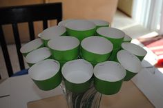 a vase filled with green cups sitting on top of a table