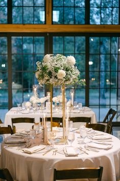 the table is set up with white flowers and candles for an elegant wedding reception in front of large windows