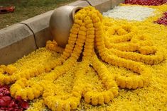 yellow and red flowers on the ground next to a metal vase with water in it