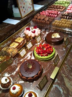 many different types of cakes and pastries on display at a bakery counter with gold trimmings