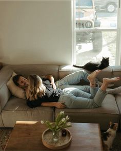 a woman laying on top of a couch next to a black and white cat in a living room