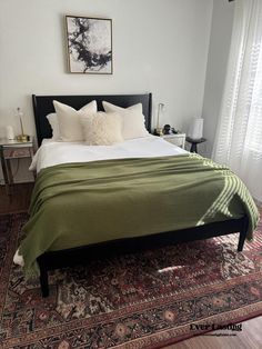 a bed with green blankets and pillows on top of it next to a rug in front of a window