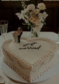 a white heart shaped cake sitting on top of a table next to a vase filled with flowers